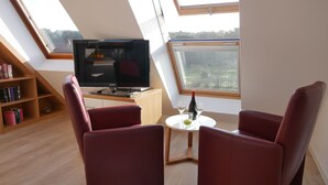A room with a TV, two red chairs, a small table with wine glasses, and a bookshelf. - APARTMENT 2 ON THE 2ND FLOOR (Norderney)