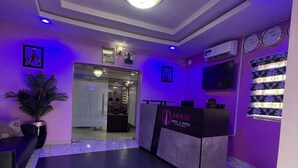 A hotel reception area with a reception desk, a potted plant, a wall-mounted TV, and a clock. - Farik Hotels and Suites  (Ibadan)