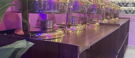 Un buffet avec plusieurs points de service, un téléviseur fixé au mur et un papier peint à motifs.