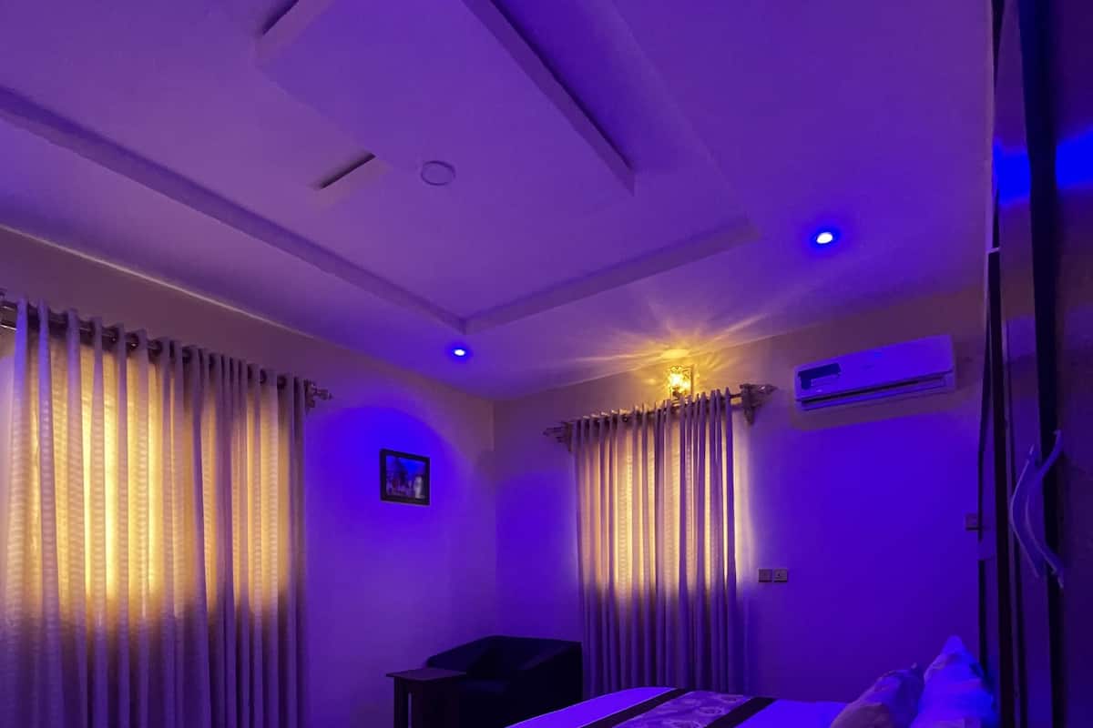 Un dormitorio con cama, cortinas, escritorio y aire acondicionado.
