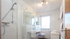 Un baño pequeño con cabina de ducha de vidrio, lavamanos y retrete.
