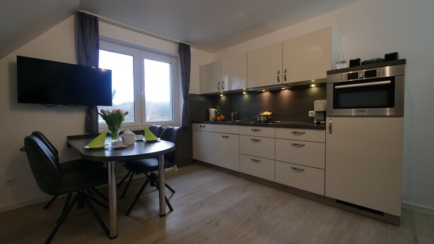 Una cocina moderna con zona de comedor, que cuenta con un televisor de pantalla plana, una cafetera y un microondas Bosch.