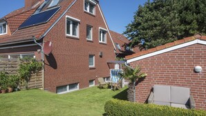 Una casa de ladrillo rojo con techo inclinado, paneles solares, patio cercado y un pequeño porche con mobiliario exterior.