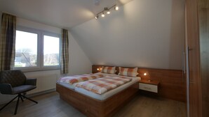Un dormitorio con una cama de madera, un escritorio y una silla. Hay una ventana con cortinas, una lámpara en el techo y un radiador.
