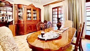 Une salle à manger avec une grande table en bois, dressée pour un repas, entourée de chaises. On aperçoit, au fond, un buffet en bois doté de portes en verre.