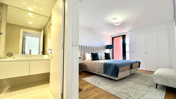 A modern bedroom with a bed, bedside table, lamp, wardrobe, and a bathroom with a mirror and sink. - One - Luxurious apartment by HD PROPERTIES (Vilamoura)