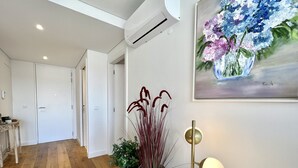 A modern interior with wooden flooring, white walls, a ceiling-mounted air conditioner, a painting of flowers, and a floor lamp. - One - Luxurious apartment by HD PROPERTIES (Vilamoura)