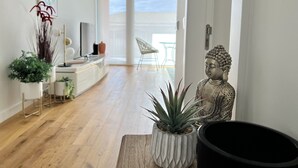 A modern living room with a wooden floor, a white sofa, a Buddha statue, and potted plants. - One - Luxurious apartment by HD PROPERTIES (Vilamoura)