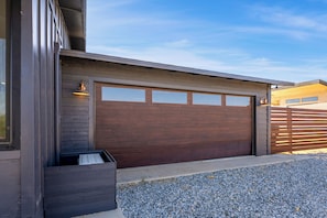 A modern garage with a large brown door, a concrete driveway, and a gravel area.