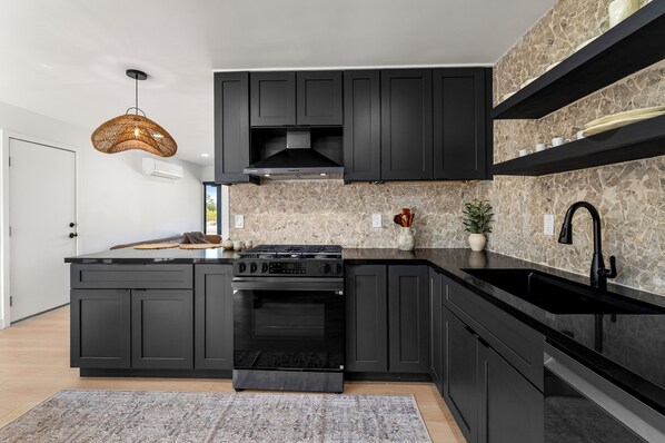 A modern kitchen with dark cabinetry, a built-in stove, and a black countertop.