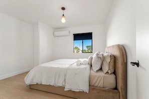 A bedroom with a bed, a window, an air conditioning unit, and a hanging light fixture.