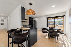 A modern kitchen with a central island, bar stools, and a large window with a view of the outdoors.