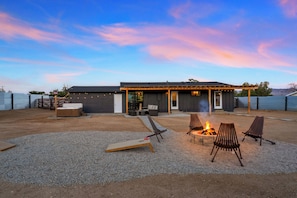 A modern outdoor patio with a fire pit, seating, and a covered area with a door.
