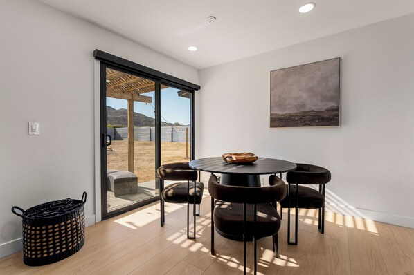 A modern interior with a round table, four chairs, a large window, and a painting on the wall.