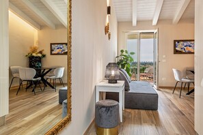 Ein modernes Interieur mit Essbereich, einem großen Spiegel, einem kleinen Tisch mit Lampe und Blick durch eine Glastür.