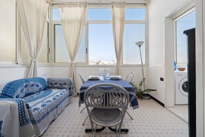 Una habitación con una mesa de comedor dispuesta para dos personas, un sofá, una silla y una lavadora.