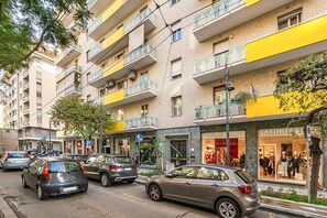 A multi-story building with balconies, a parking area, and storefronts.