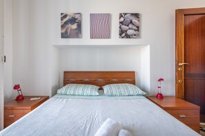Une chambre à coucher avec un lit en bois, deux tables de chevet, une petite table et trois œuvres d’art accrochées au mur.