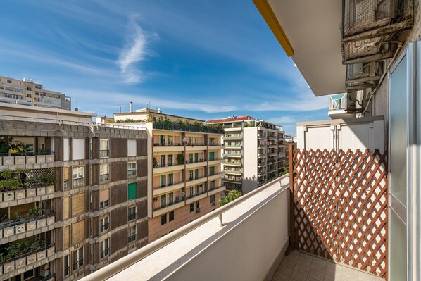 A balcony with a view of multi-story buildings, a lattice fence, and a clear sky.