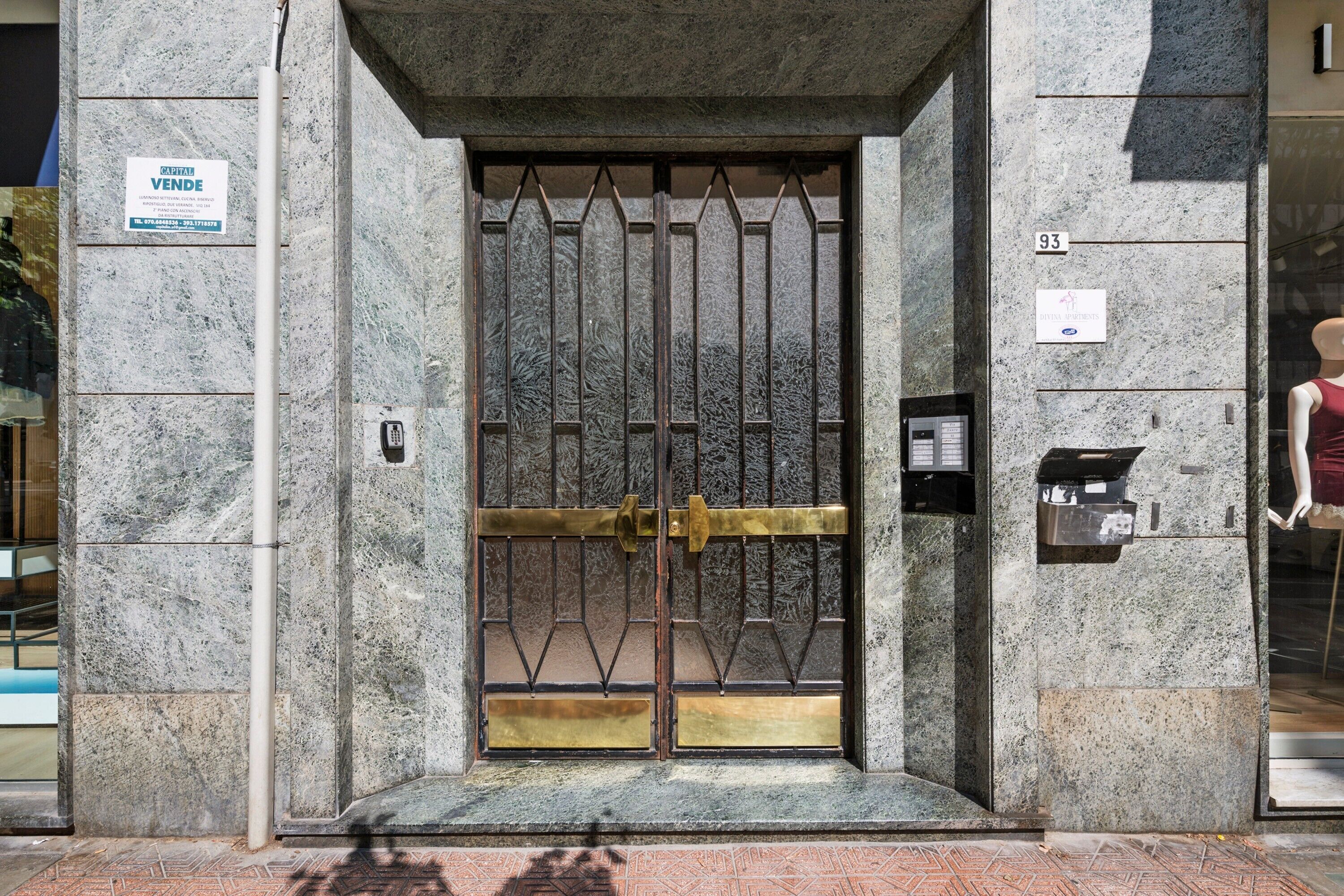A building entrance with a metal gate, a telephone, and a sign indicating 'DIVINA APARTMENTS'.