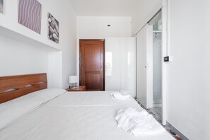 A hotel room with a wooden bed, a nightstand, a white wall, and a door leading to another room.