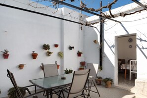 A glass table with chairs, potted plants on the wall, and a white chair in the doorway. - Vacation Home "Las Niñas" with Sea View, Private Terrace & Garden (Vejer de la Frontera)