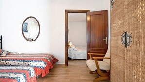 A bedroom with two beds, a wooden wardrobe, a chair, a mirror, and a door leading to another room.