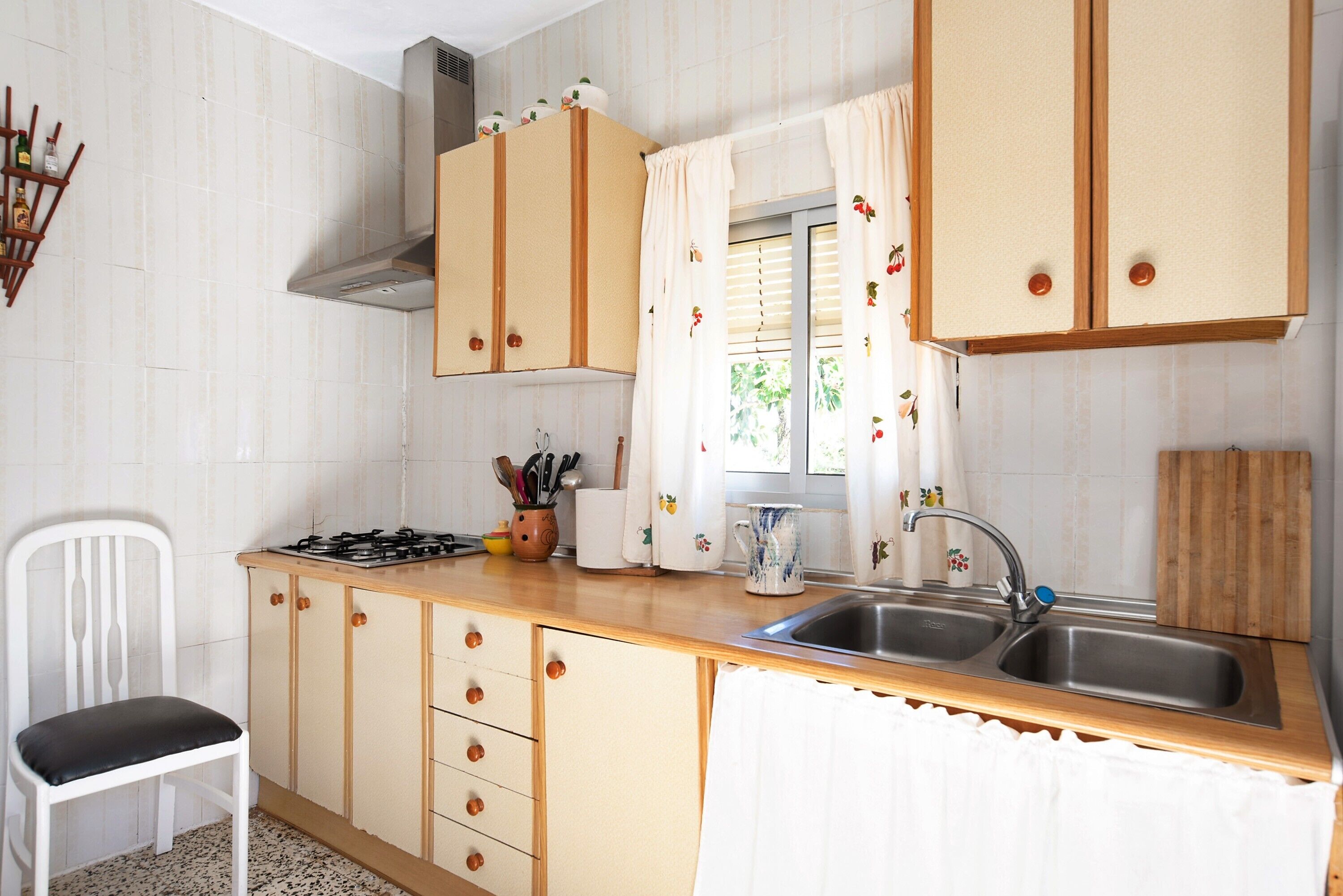 A kitchen with wooden cabinets, a gas stove, a sink, and a window with curtains.