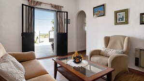 A living room with a sofa, armchair, and coffee table, a door leading outside, and framed pictures on the wall.