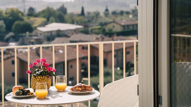 Ein Balkon mit einem Tisch, gedeckt für ein Frühstück, darunter Obst, ein Croissant und Orangensaft.