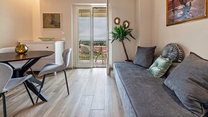 Ein modernes Wohnzimmer mit einer Couch, einem Esstisch mit Stühlen, einer Balkontür und einem Bild an der Wand.