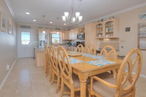 Enjoy meals with friends and family in this dining area, featuring a long table and a well-equipped kitchen.