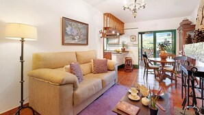Una sala de estar con un sofá, una lámpara de pie, una mesa de comedor con sillas y vistas a través de una puerta.
