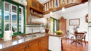 Una cocina con armarios de madera, un lavamanos, una cafetera y una zona de comedor con sillas y una mesa.