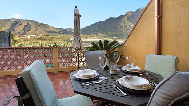 Mesa para dos con platos, cubiertos y copas de vino, con vistas a un paisaje montañoso.
