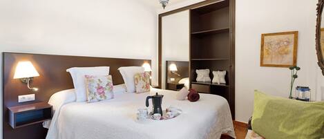 Un dormitorio ordenado con cama, lámparas de noche, cafetera y estante con toallas.