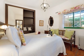 A room with a bed, a bench, a radiator, a window with a view, a mirror, and a shelf.