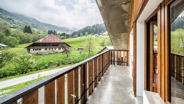A balcony with a view of a green valley, a red-roofed building, and a cloudy sky. - Apartment 'Coeur De Charmy' with Mountain Views and Wellness Spa (Abondance)