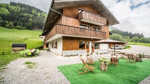 A two-story wooden house with a balcony, outdoor seating, and a gravel driveway. - Apartment 'Coeur De Charmy' with Mountain Views and Wellness Spa (Abondance)