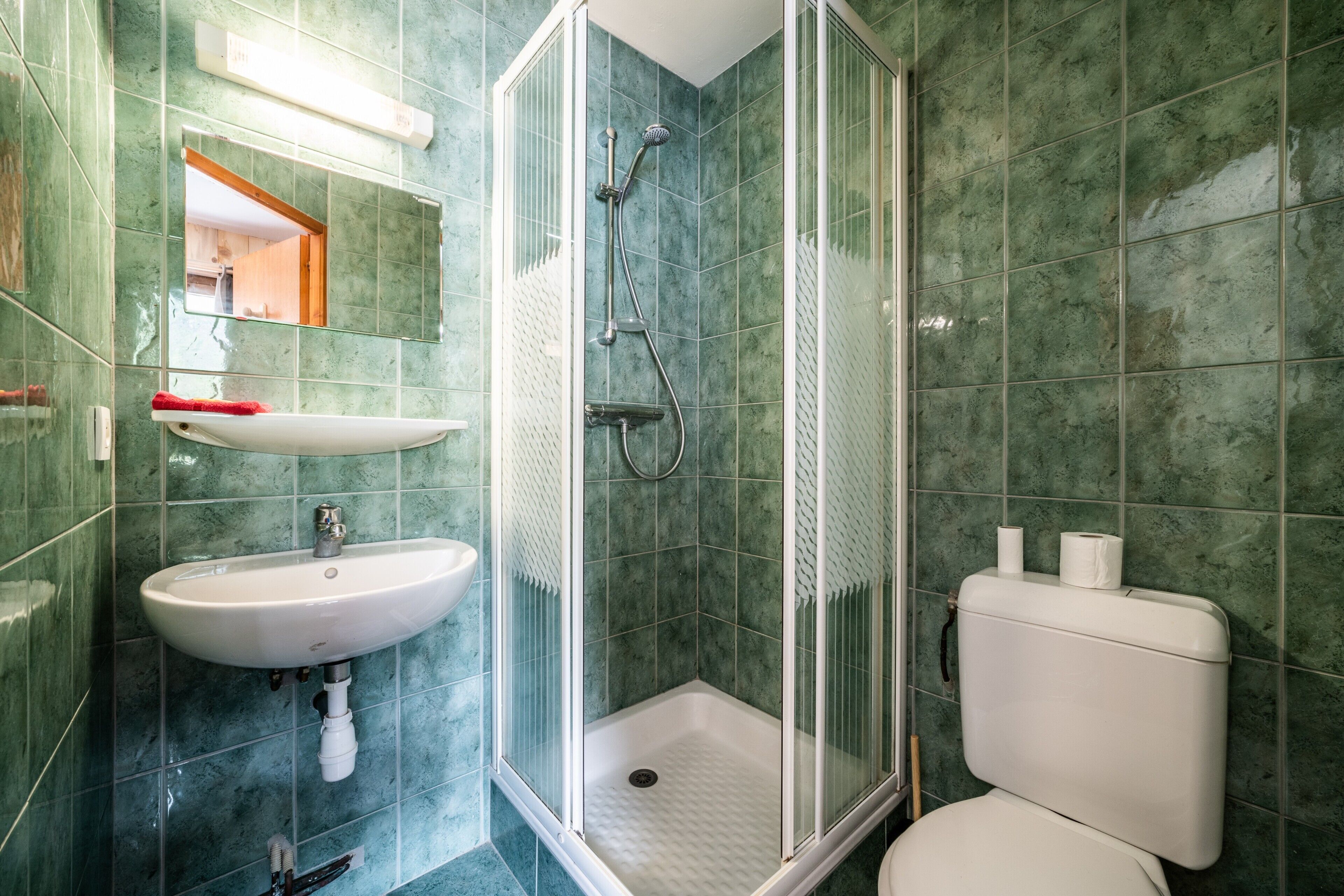 Un baño con ducha, lavamanos, inodoro y espejo.