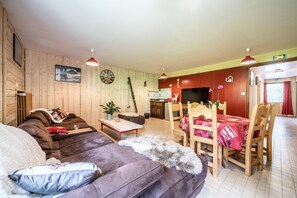 Una habitación acogedora con sofá, una mesa de comedor con sillas, un reloj en la pared y piso de madera.