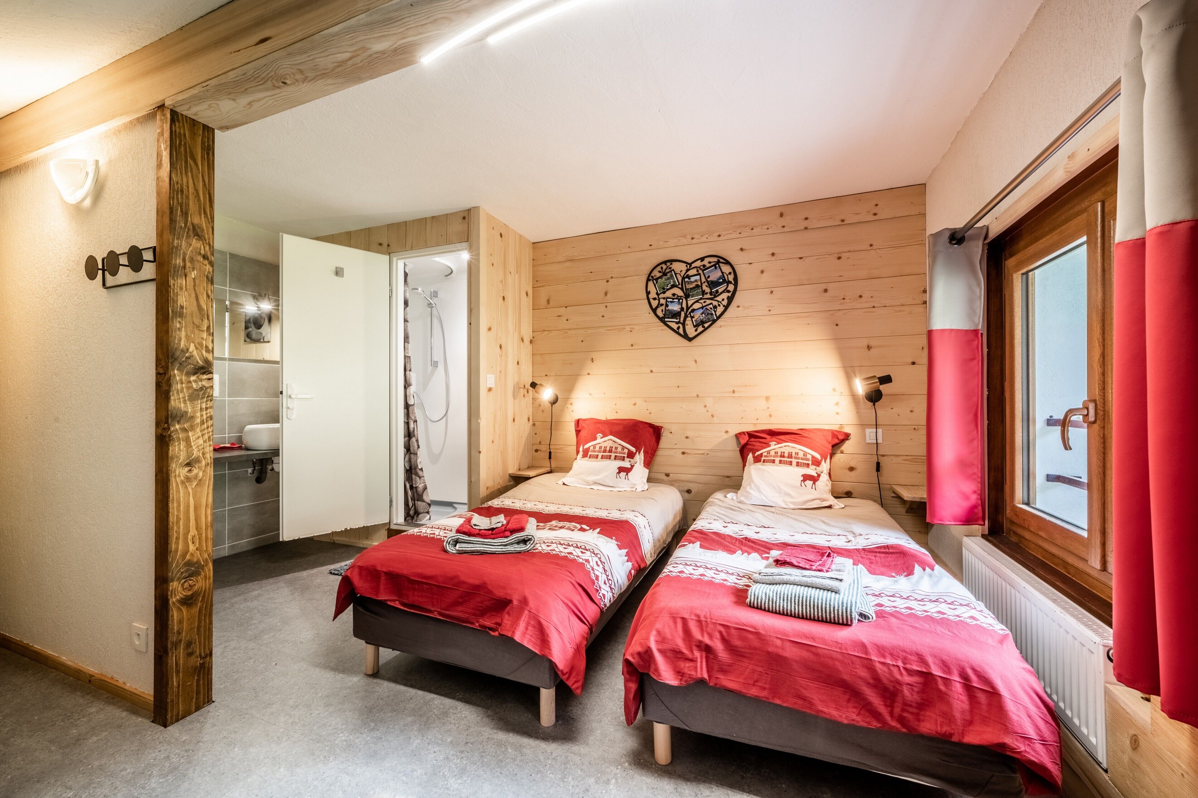 Een kamer met twee bedden, houten wanden, een hartvormige decoratie en een raam met gordijnen.