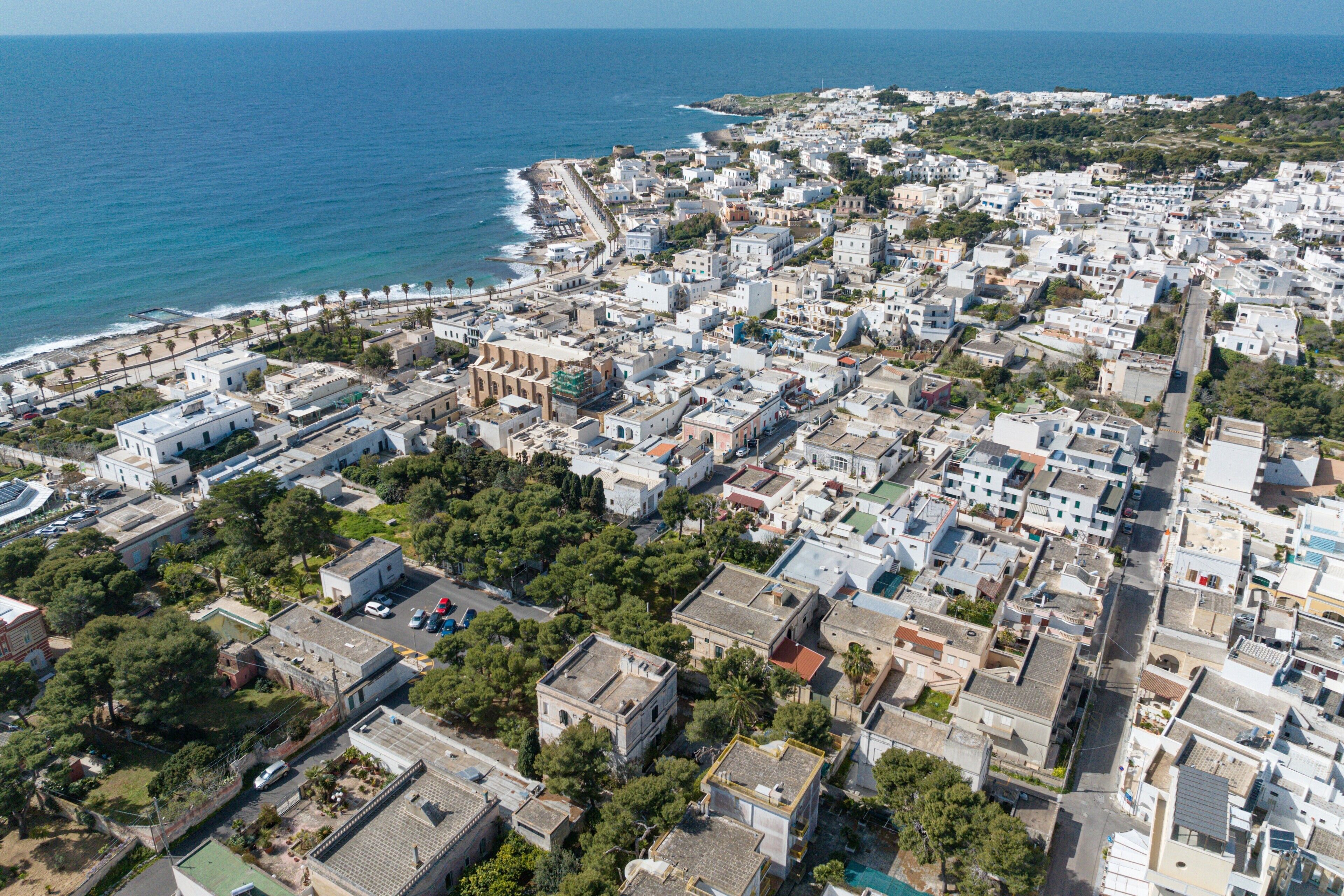 Luftaufnahme einer Küstenstadt mit weißen Gebäuden, einem Strand und freiem Blick auf das Meer.