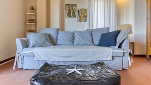 A living room with a grey sofa, a black leather ottoman, a white lamp, and wall art.