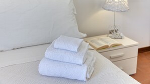 A neatly made bed with white linens, a white bedside table with a lamp, and an open book.