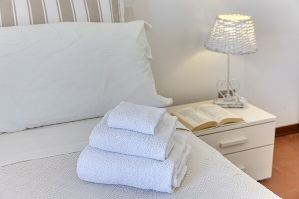 A neatly made bed with white linens, a white bedside table with a lamp, and an open book.