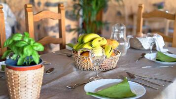 A dining table set with plates, cutlery, a glass, a basket of fruit, and a potted plant.