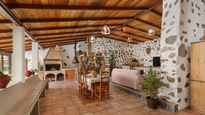 A rustic interior with a stone wall, wooden ceiling beams, a stone fireplace, and a dining table with chairs.