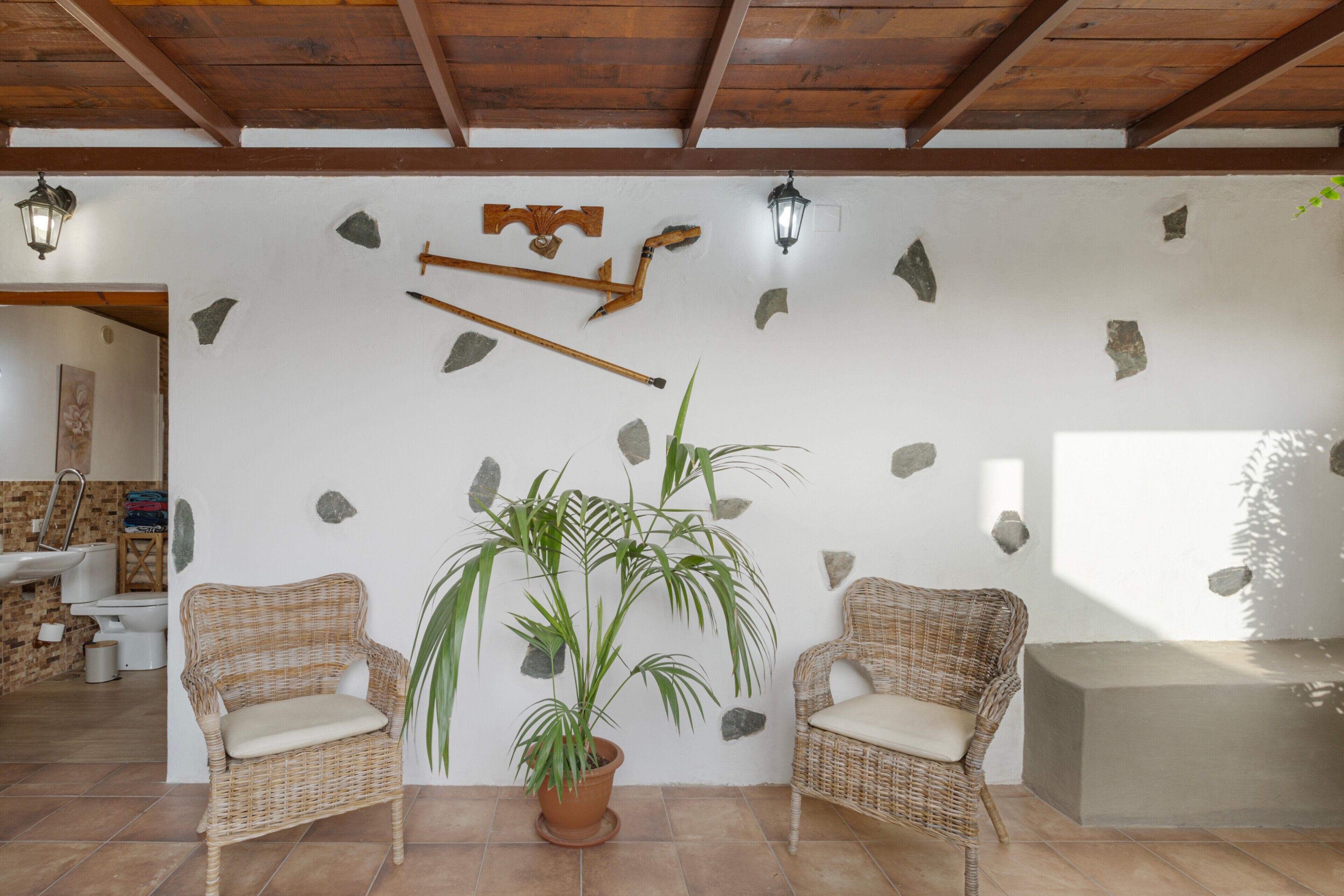 A room with two wicker chairs, a potted plant, and stone wall decorations.