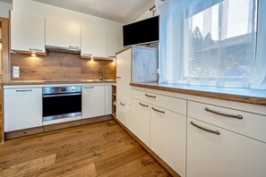 Una cocina moderna con armarios blancos, horno integrado y una ventana con cortinas translúcidas.